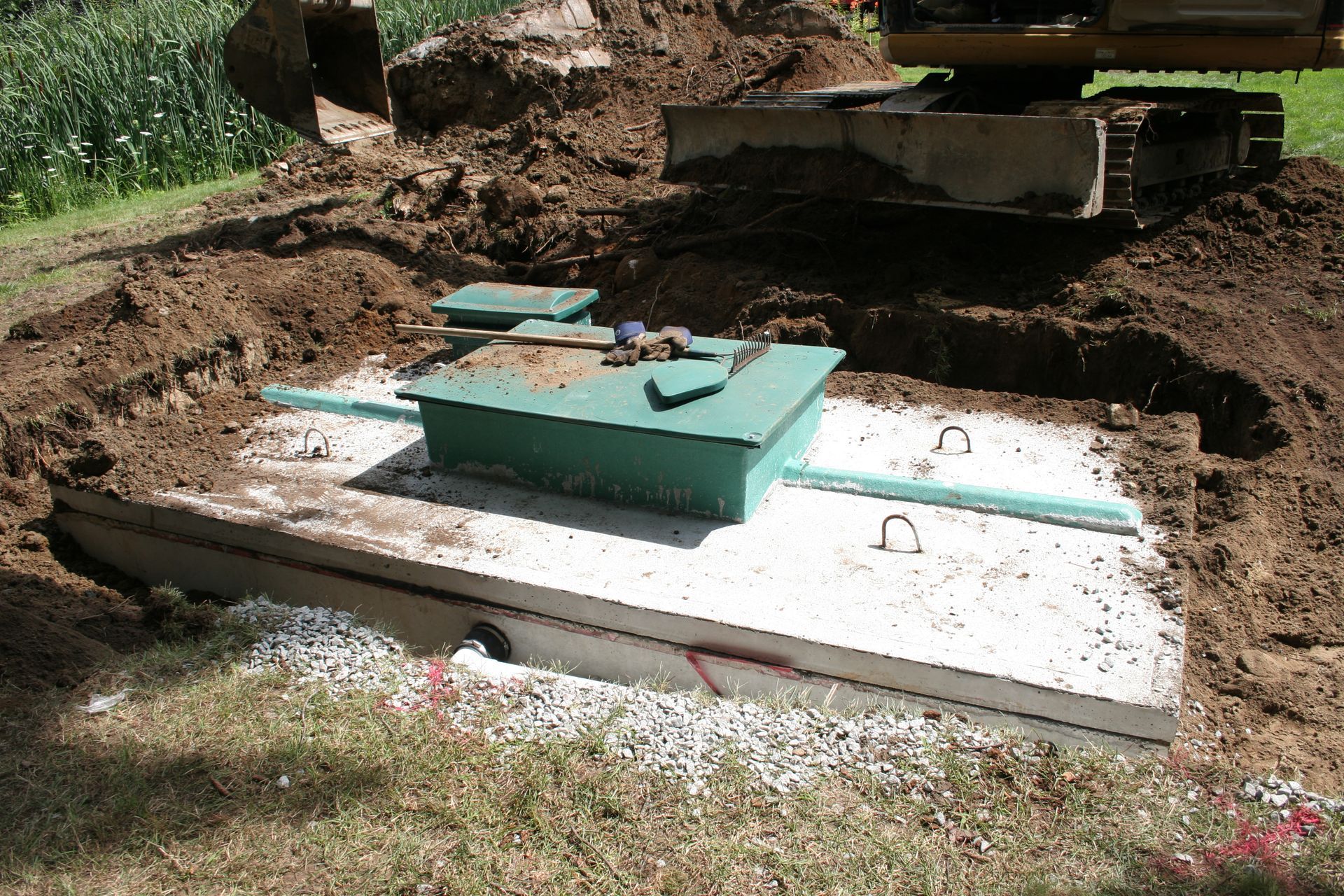 Septic tank installation in progress; green tank, excavator, and dirt.