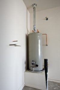 A tall, gray water heater in a corner of a white-walled room with a vent pipe.