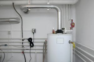 White water heater with silver ductwork, pipes, and electrical wiring on a white wall.