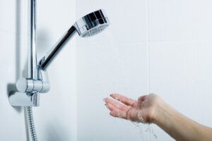 Hand testing water flow from a chrome shower head in a white-tiled bathroom.
