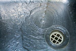 Water flows into a stainless steel sink, visible drain, and water droplets.