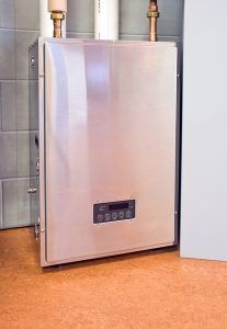 Silver water heater with digital display, copper pipes, and white/gray walls on an orange floor.