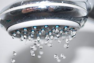 Shower head with water droplets falling. Chrome fixture, white background.