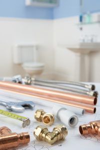 Plumbing tools and pipes on a blueprint, bathroom in the background.