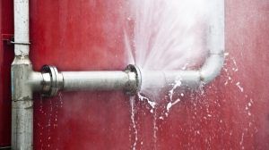 Water gushing from a broken pipe connection, spraying onto a red wall.