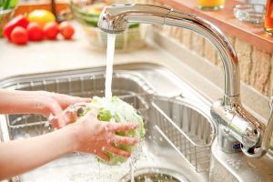 Person washing a head of lettuce under a running faucet in a kitchen sink.