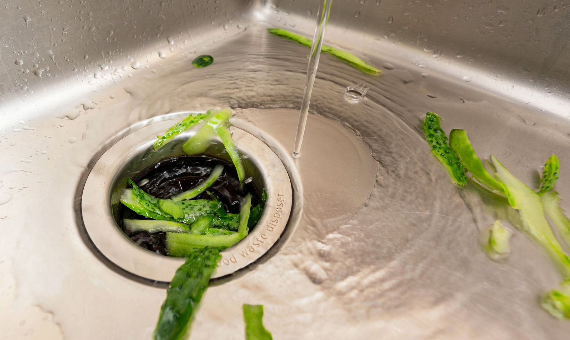 Kitchen garbage disposal grinding food scraps with running water to prevent clogs in Olympia, WA.