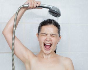 Woman in shower, screaming, holding showerhead over her head; water pouring down.