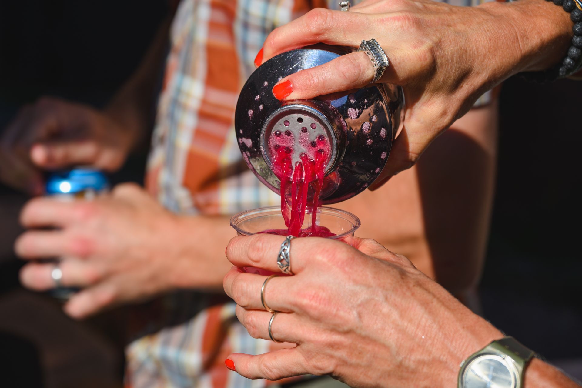 hands pouring a red drink out of a cocktail shaker