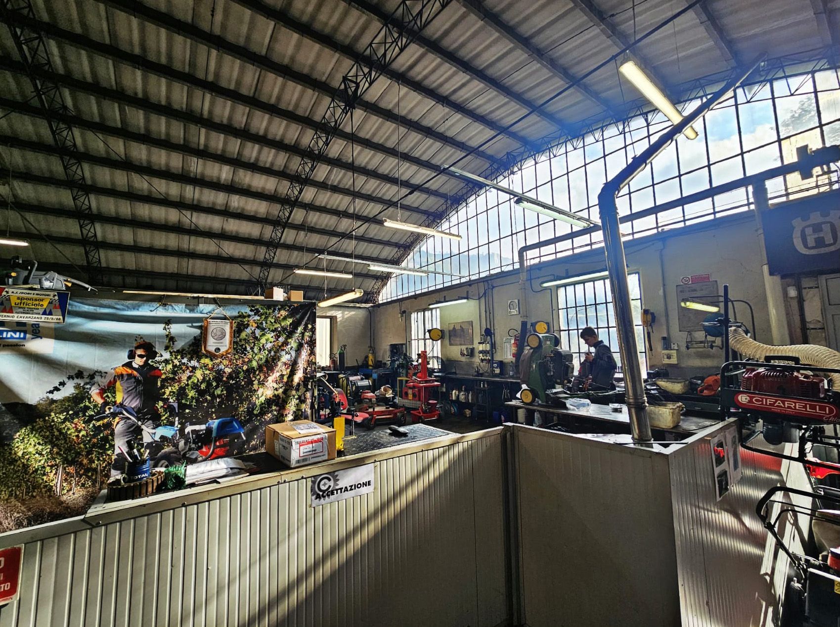 Interno di un'officina con persone al lavoro, soffitto metallico e attrezzi.