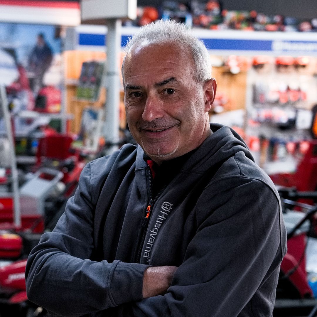 Uomo con i capelli grigi e le braccia incrociate, sorridente, in un negozio di macchinari e utensili.