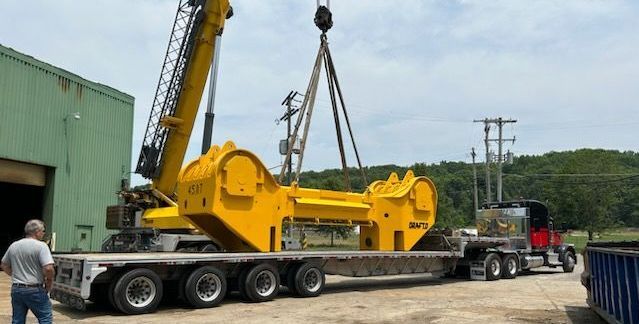 A crane is lifting a large yellow object on top of a semi truck.