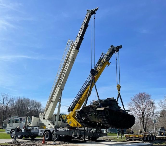 Two cranes are lifting a tank in a park