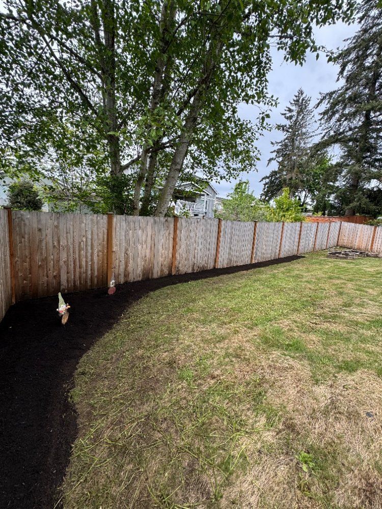 Backyard with a wooden fence and a freshly mulched garden bed edging the grass.