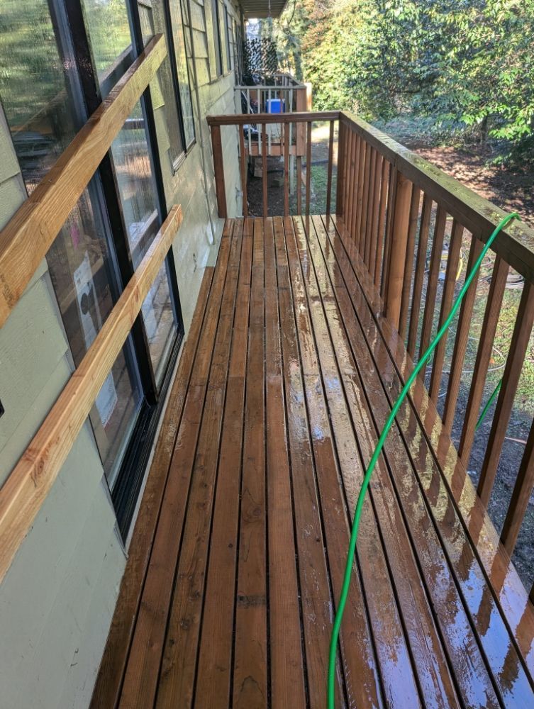 Narrow wooden deck with brown railing, green hose, and surrounding trees.
