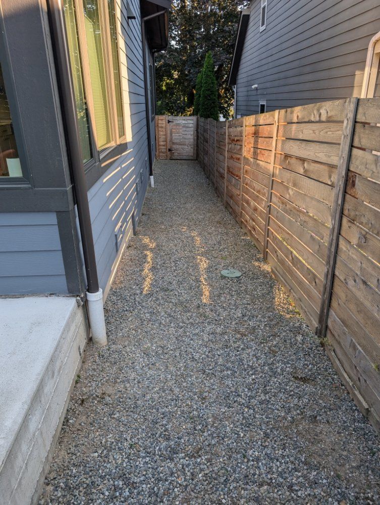 Gravel path between two buildings with a wooden fence on the right side.