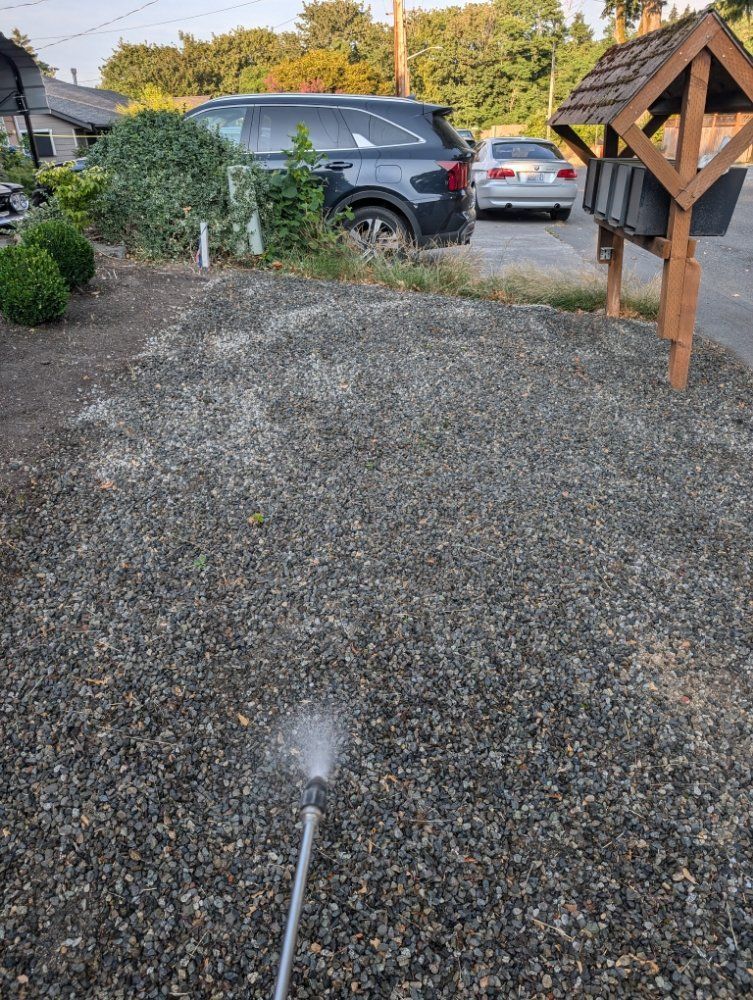 A person spraying water on a gravel driveway next to a mailbox.
