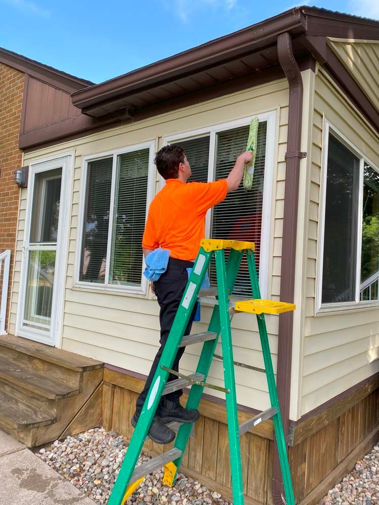 A man is standing on a ladder cleaning a window.