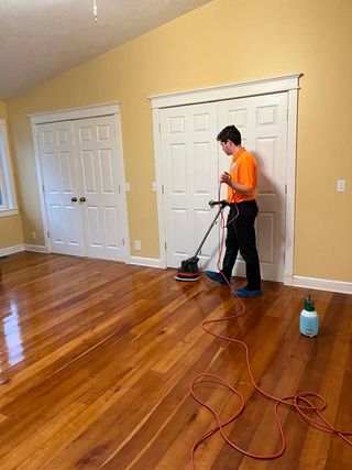 A man is cleaning a hardwood floor with a vacuum cleaner.