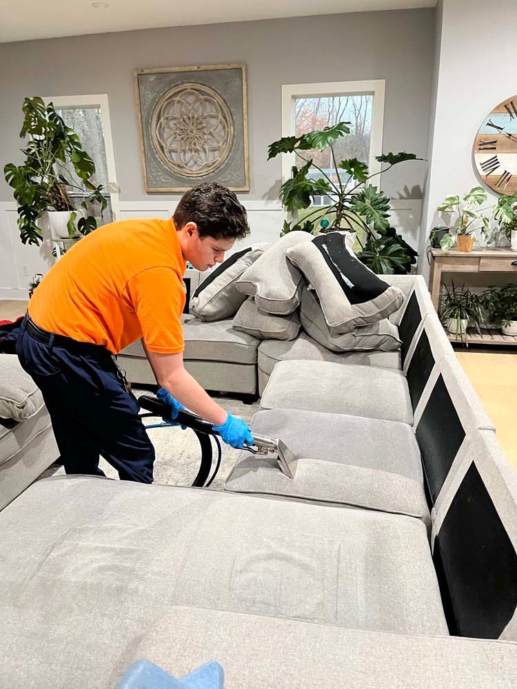 A man is cleaning a couch in a living room with a vacuum cleaner.