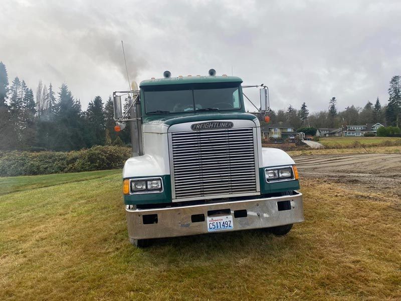 Green and white semi-truck on grassy field; smoke from exhaust. Cloudy sky.