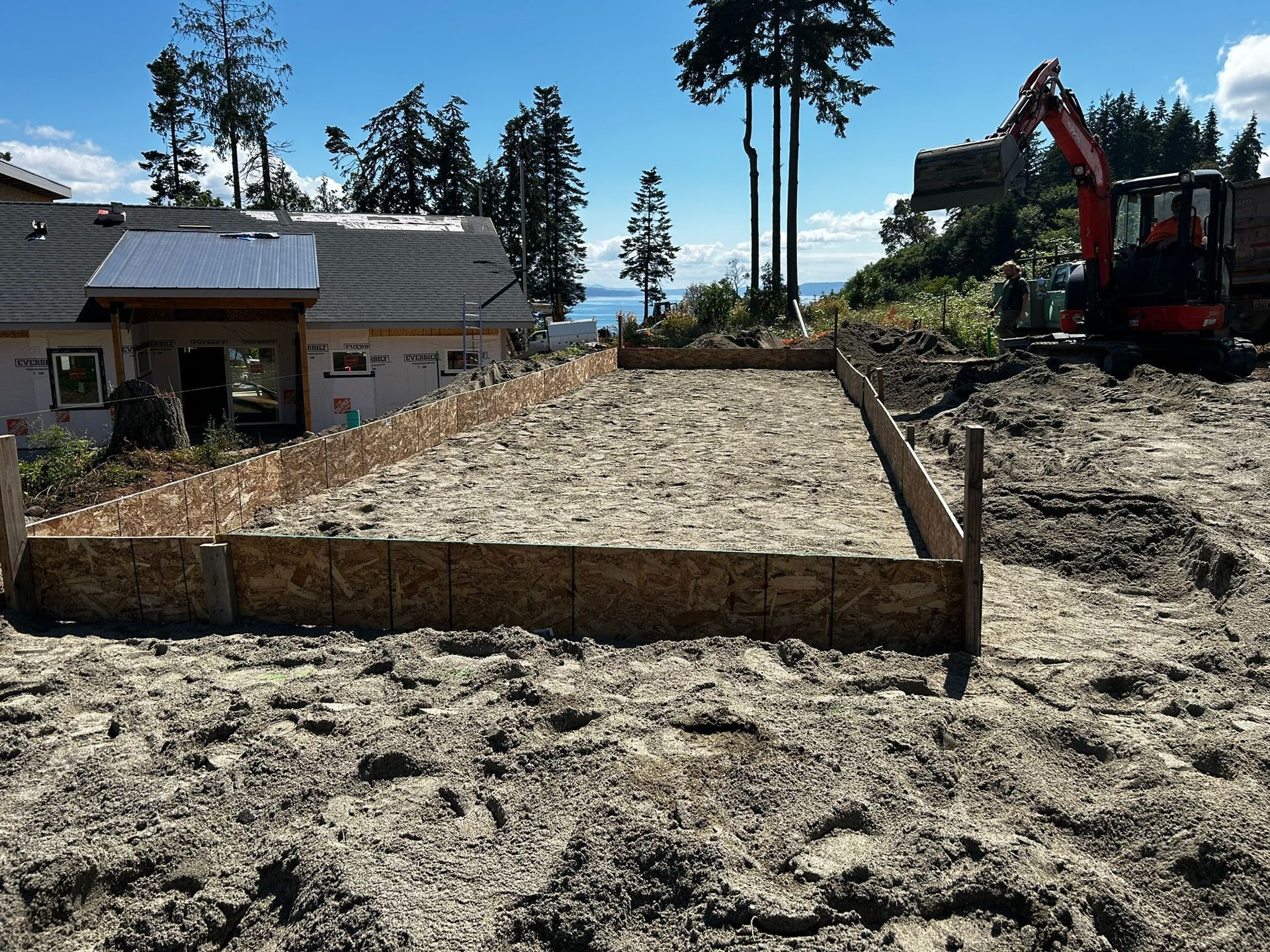 Foundation formwork constructed on sandy ground with excavator in the background, house under construction.