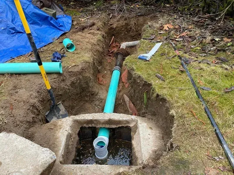 A plumbing repair site with an open pit, pipes, and tools in a yard.