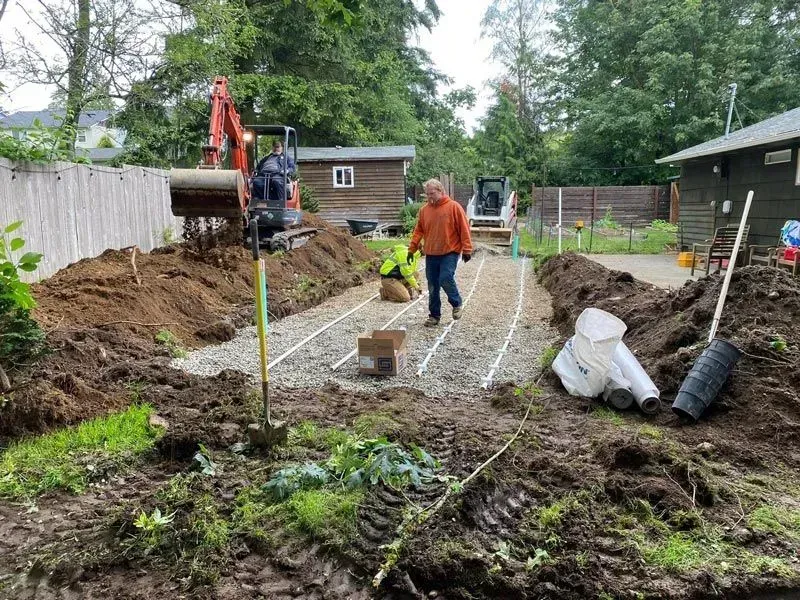 A plumbing repair site with an open pit, pipes, and tools in a yard.