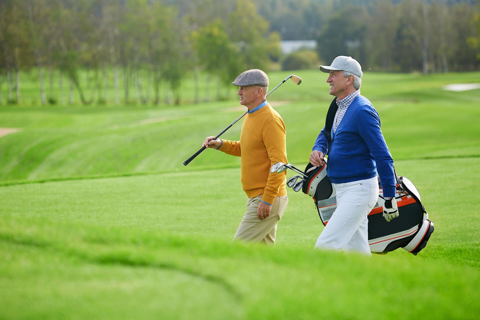 two men are walking on a golf course carrying golf clubs .