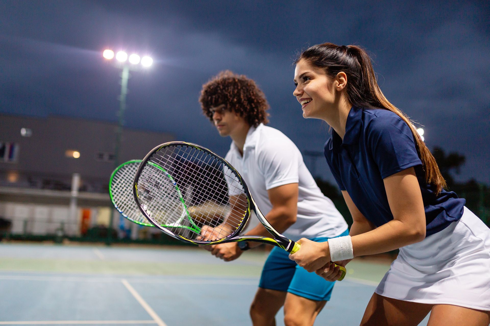 a man and a woman are playing tennis on a tennis court at night.