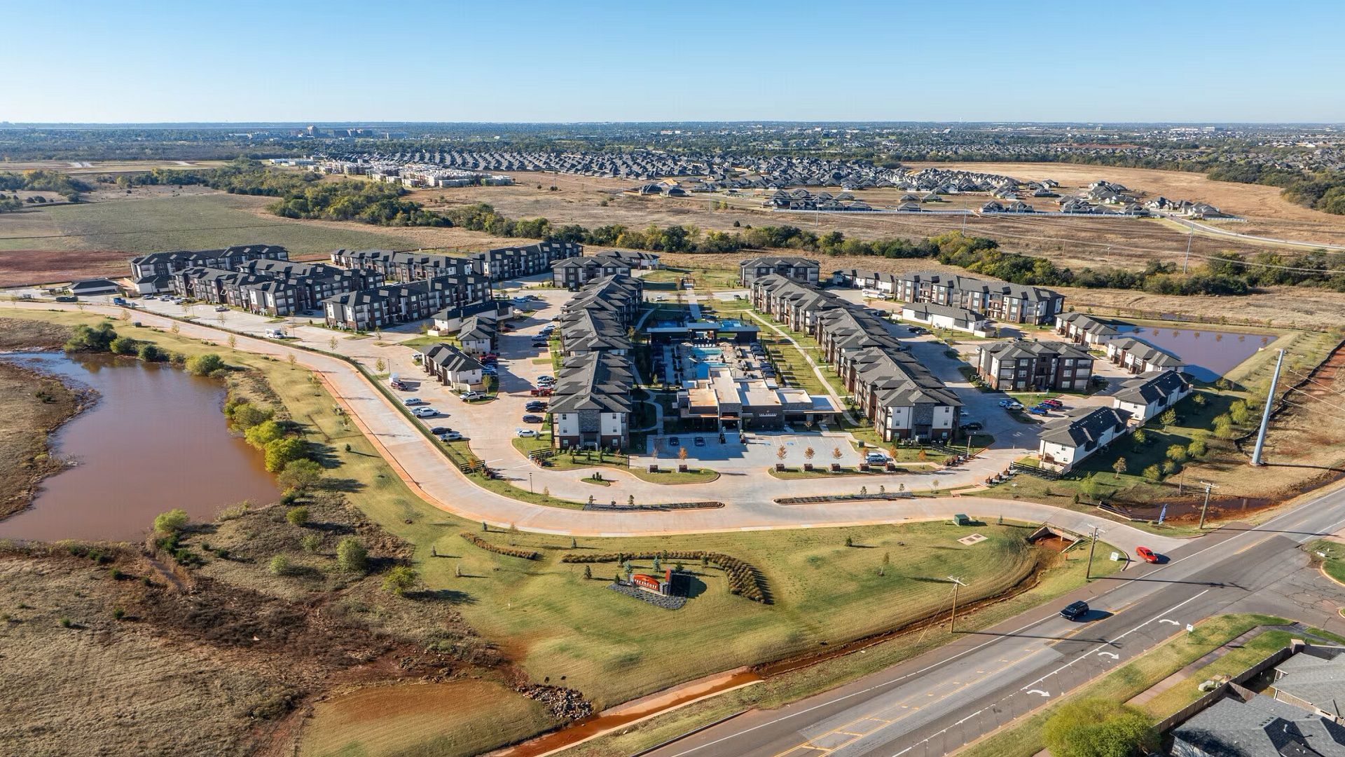 Aerial view of apartment complex with ponds and surrounding fields. Red dirt and blue sky.