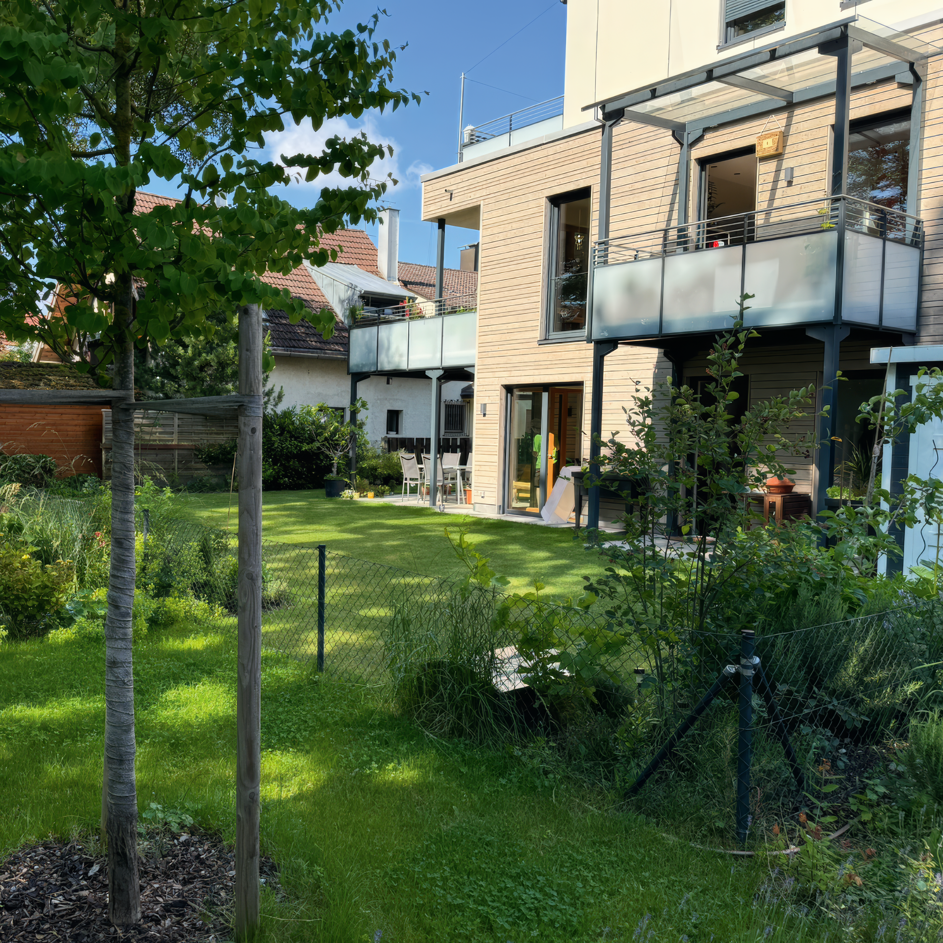 Eine Rasenfläche mit jungen Bäumen, umgeben von Grün, und ein modernes Backsteingebäude.