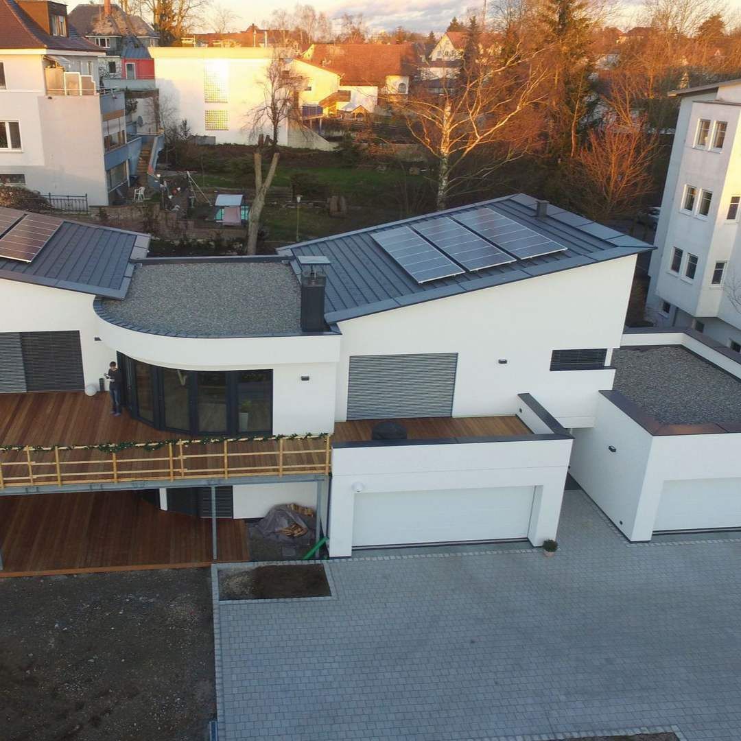 Modernes weißes Haus mit Solarpaneelen auf dem Dach und einer Holzterrasse.