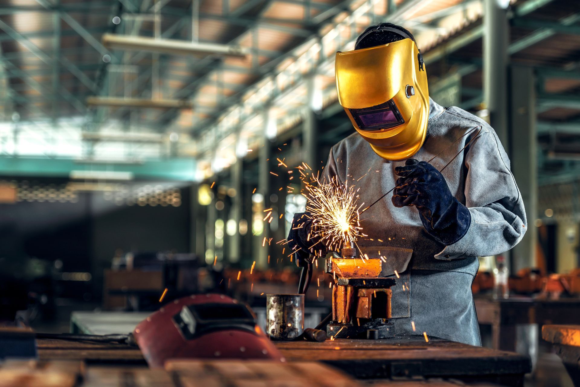 A man wearing a welding helmet is welding a piece of metal in a factory.