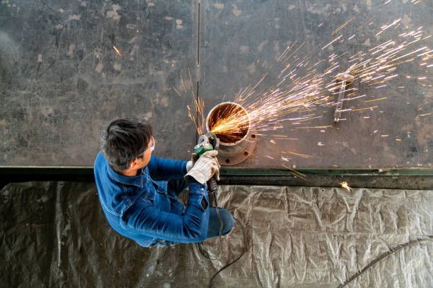 A man is cutting a metal pipe with a grinder.