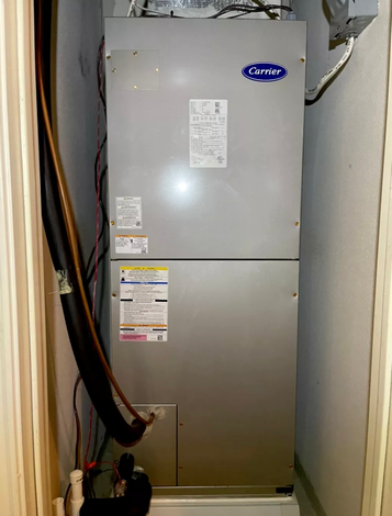 Carrier HVAC unit in a utility closet. Gray metal, with ductwork and wiring.