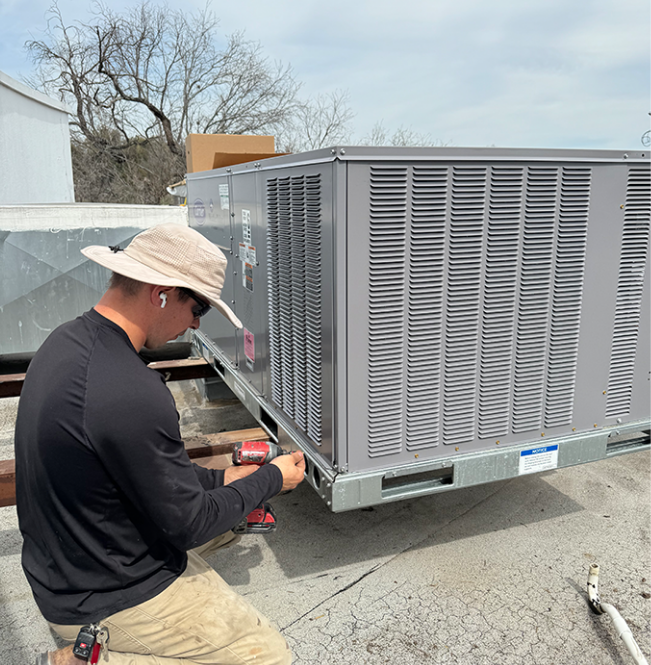 A person installing an air conditioning unit on a rooftop.