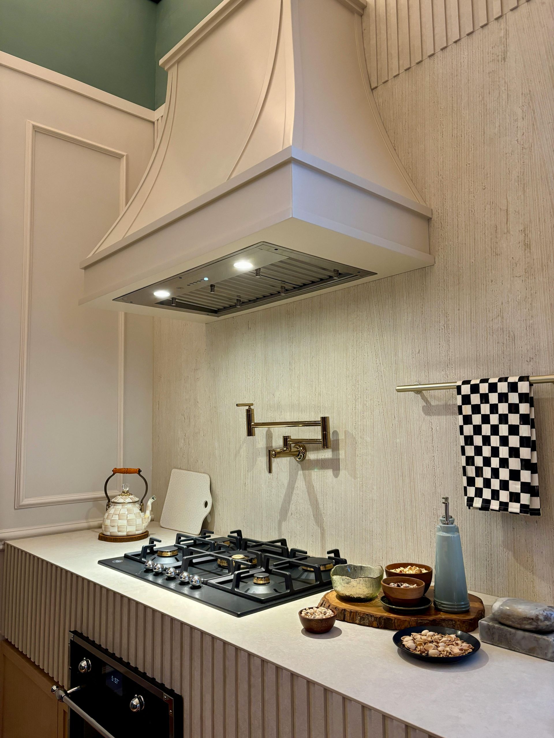 Kitchen with stove, range hood, and backsplash. Features a wall-mounted pot filler and cooking accessories.