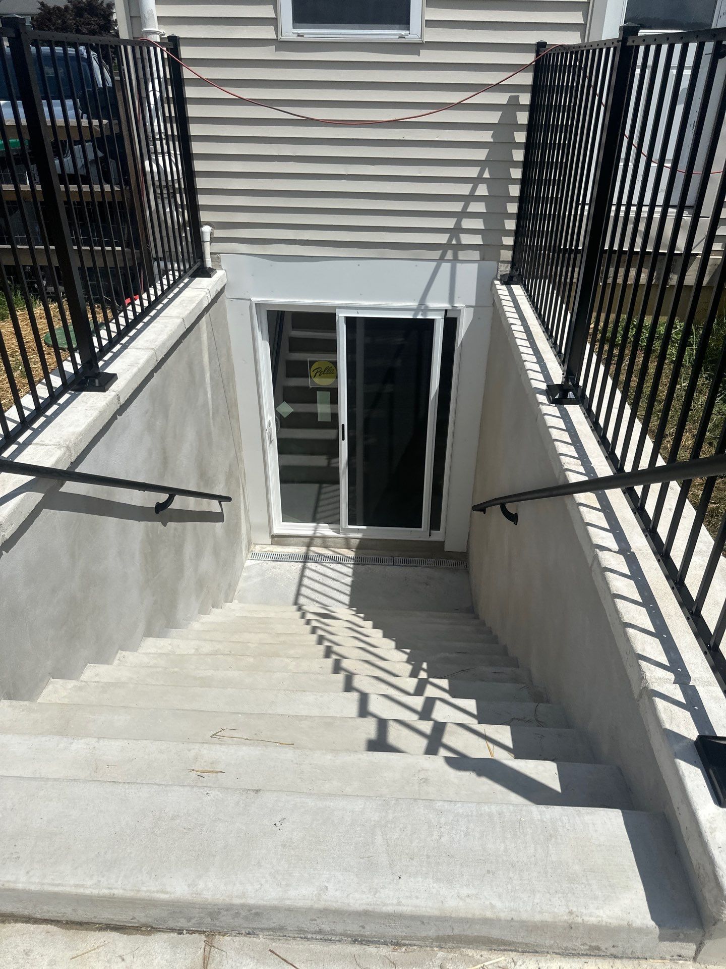 Stairway leading down to a glass sliding door entrance. Concrete stairs with black railings.