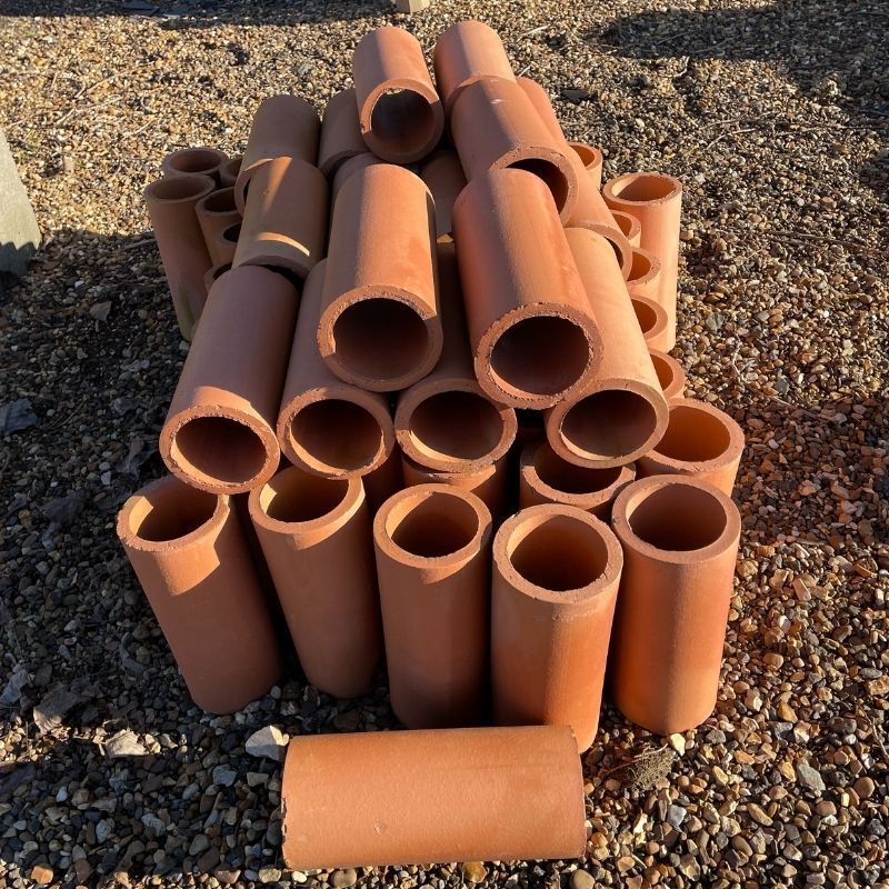 Pile of terracotta chimney flue pipes on a gravel surface.