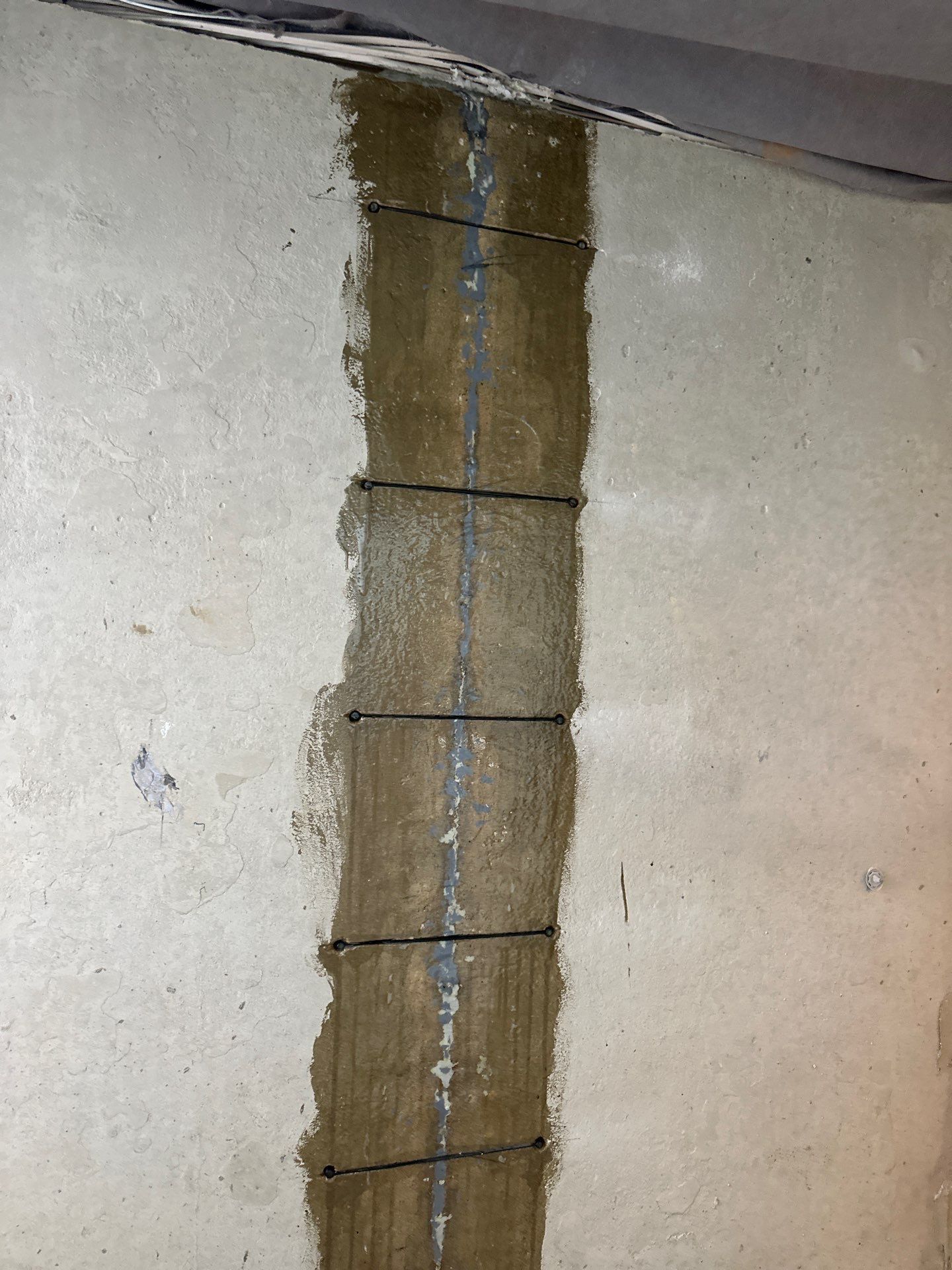Concrete floor with a wet, dark brown line running down the middle. Black lines are visible across the brown stain.