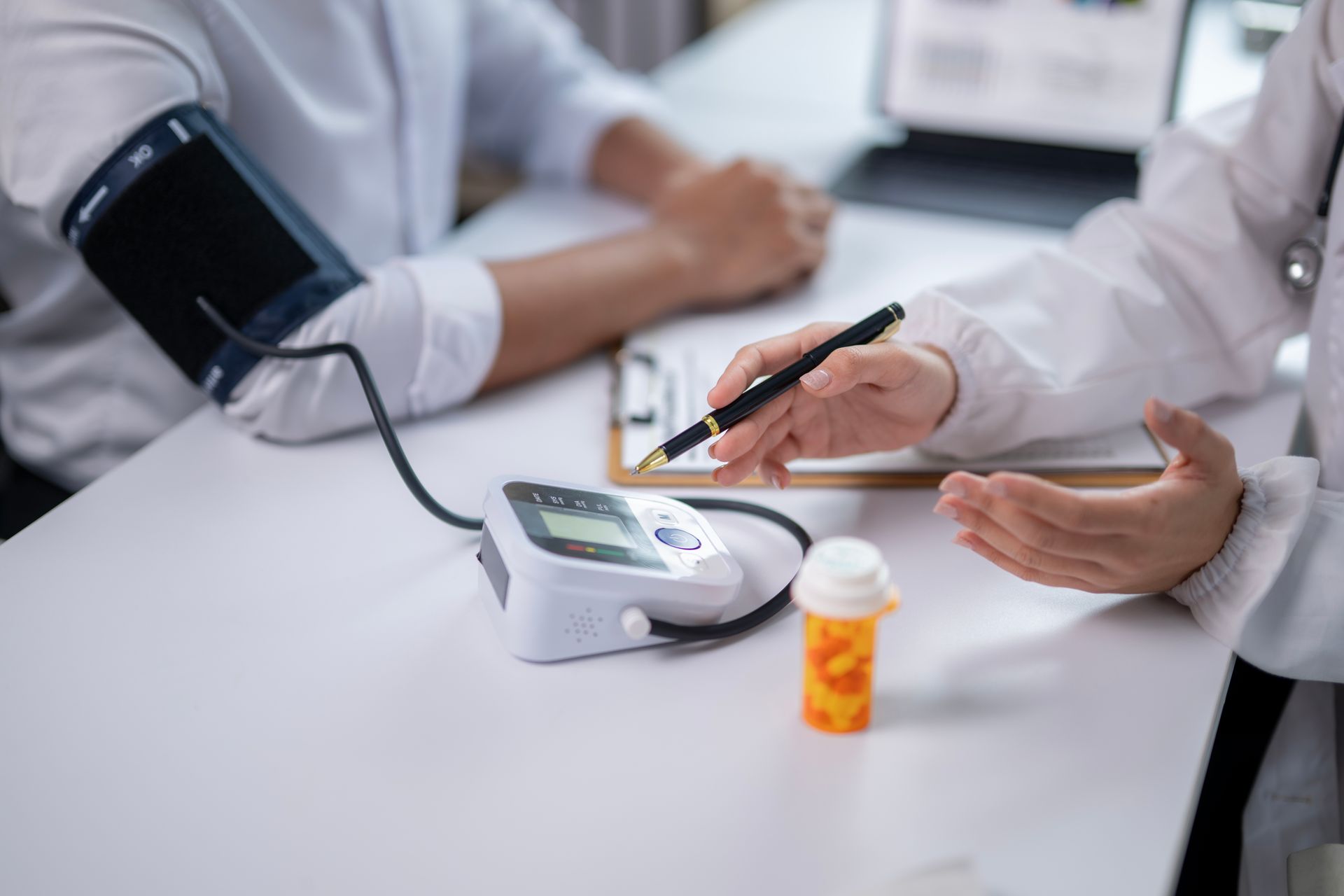 Doctor taking a patient's blood pressure; a monitor and medication are on the table.