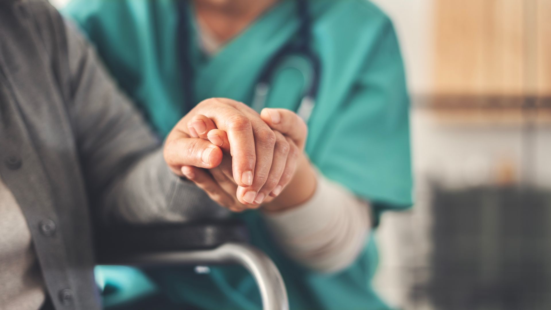 A person in a wheelchair holds hands with a medical professional wearing scrubs.