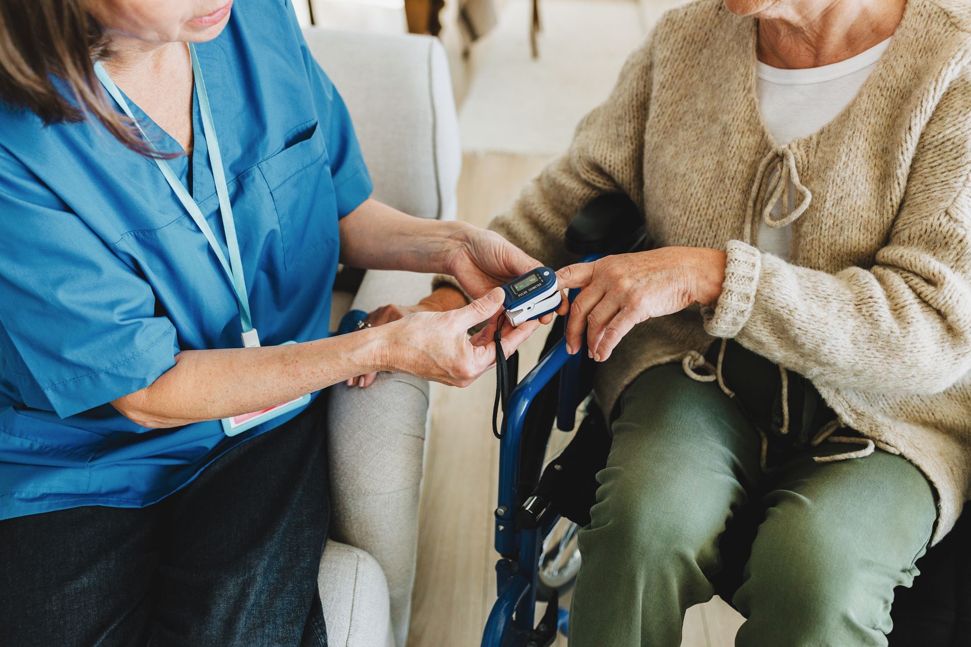Nurse using a pulse oximeter on a person's finger, indoors.