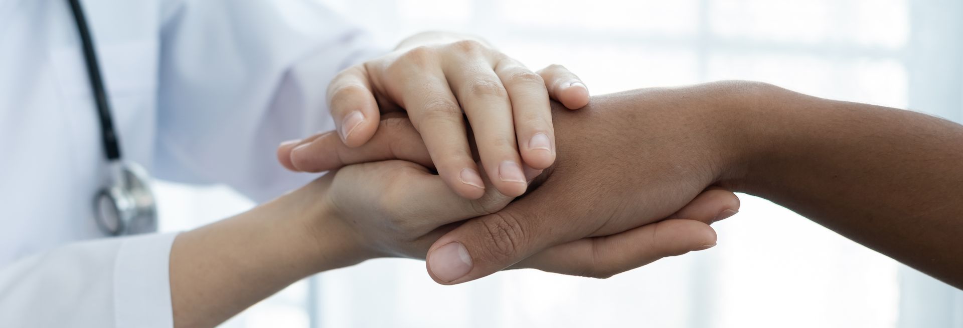 Doctor's hand holding a patient's hand for comfort, soft lighting.