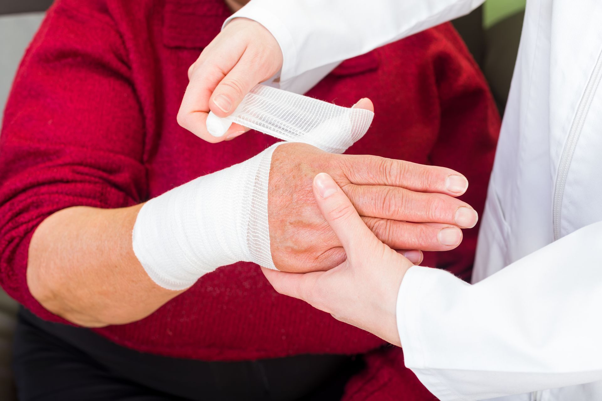 Person's injured hand being wrapped with a bandage by another person in a white coat.