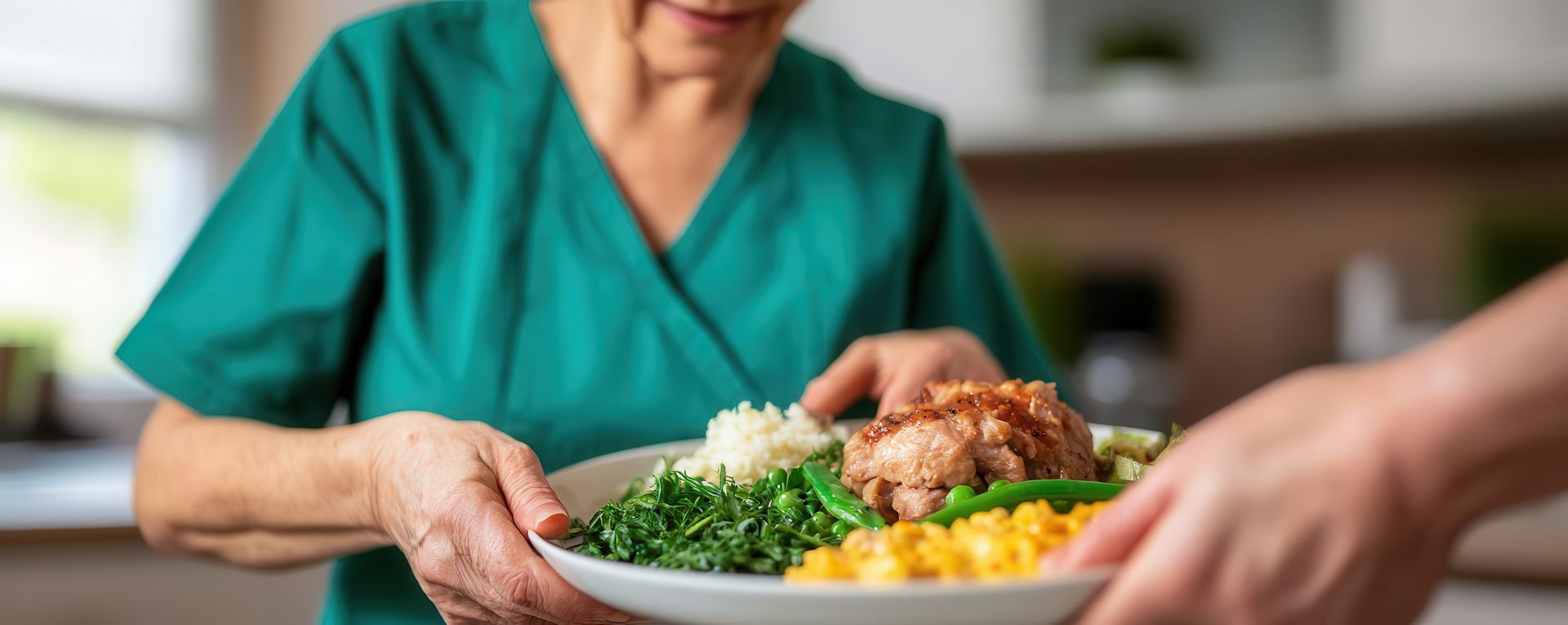 Person in green scrubs passing a plate of food to another person.