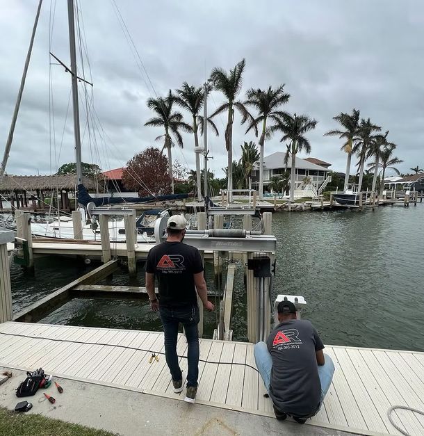 Two men working on a boat dock, cloudy sky, palm trees, canal with houses and boats.