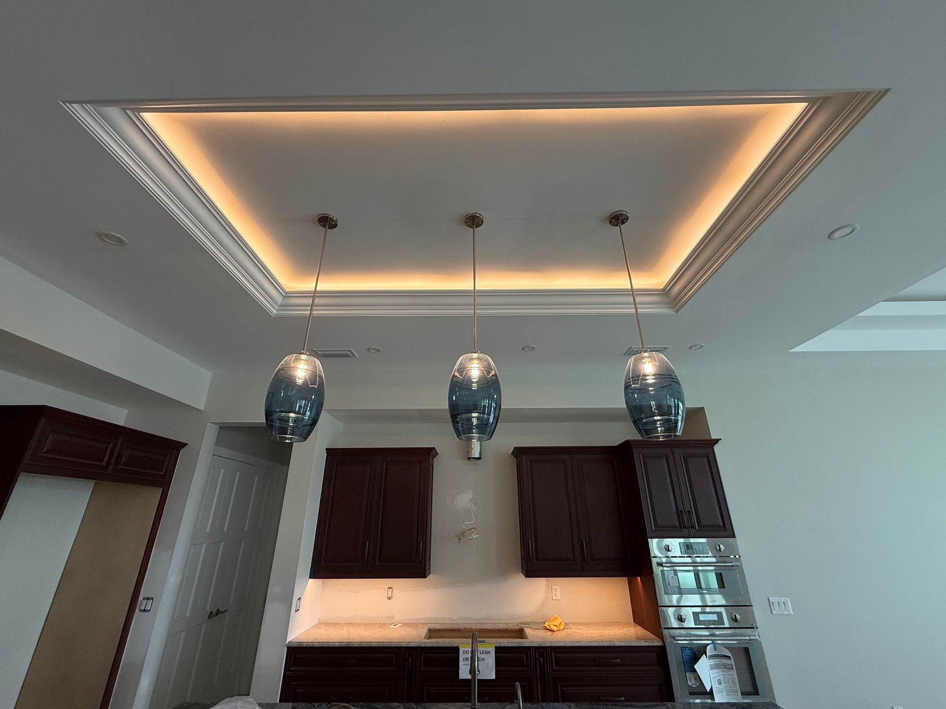 Kitchen with dark cabinets, three pendant lights, recessed ceiling lighting.