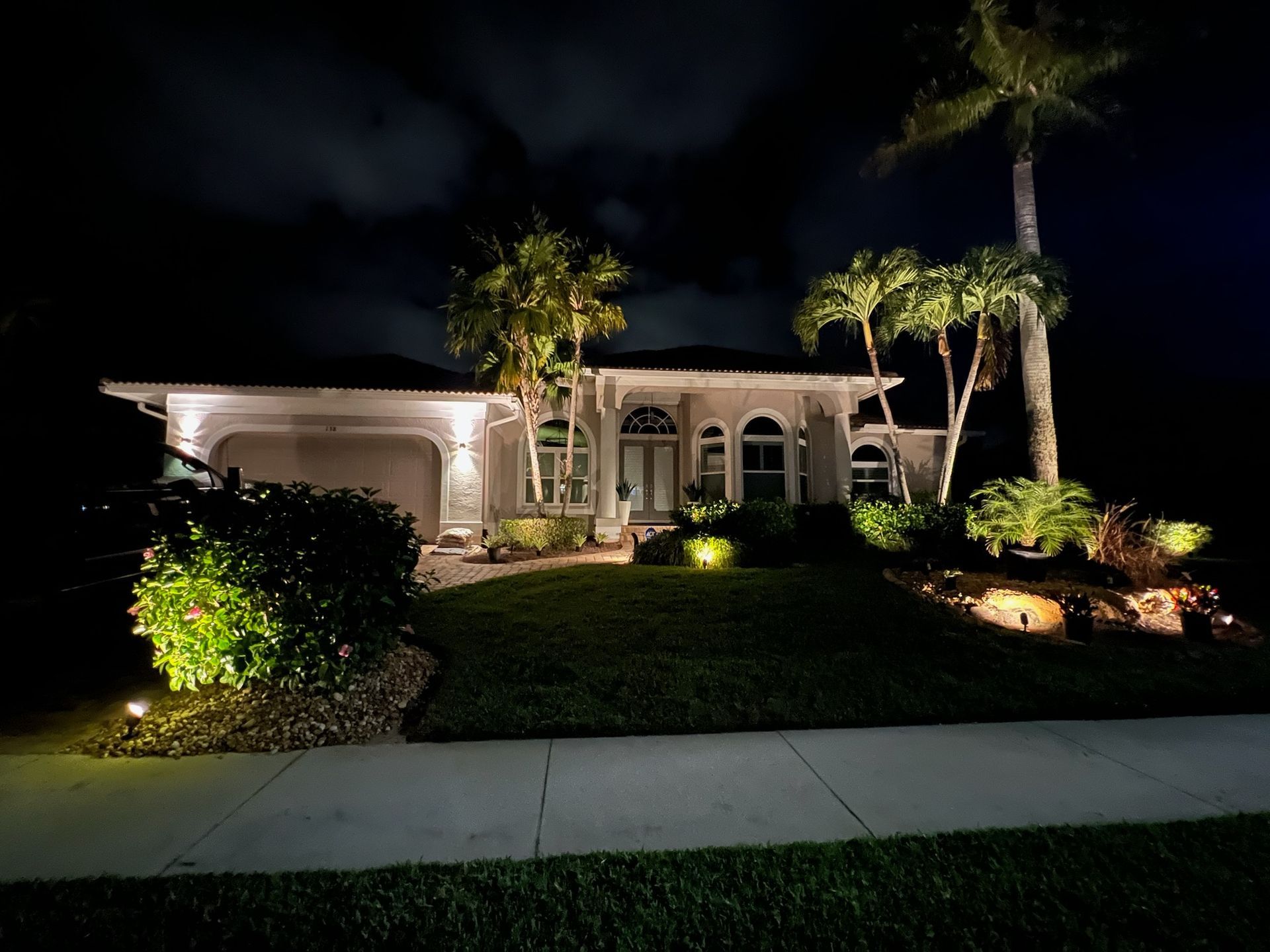 A well-lit house at night with landscape lighting illuminating the front yard, trees, and exterior.
